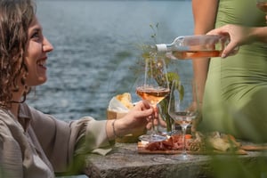 Une jeune femme sourit à son amie qui lui sert du vin rosé pendant l'apéritif