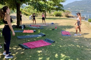Gruppo di donne con tappetini da yoga fanno workout sul lago