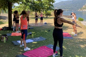 Gruppo di donne con tappetini da yoga fanno workout sul lago