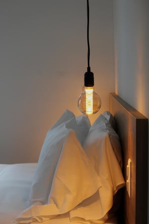 Lampada a sospensione accesa sopra il letto in una camera dal design essenziale.